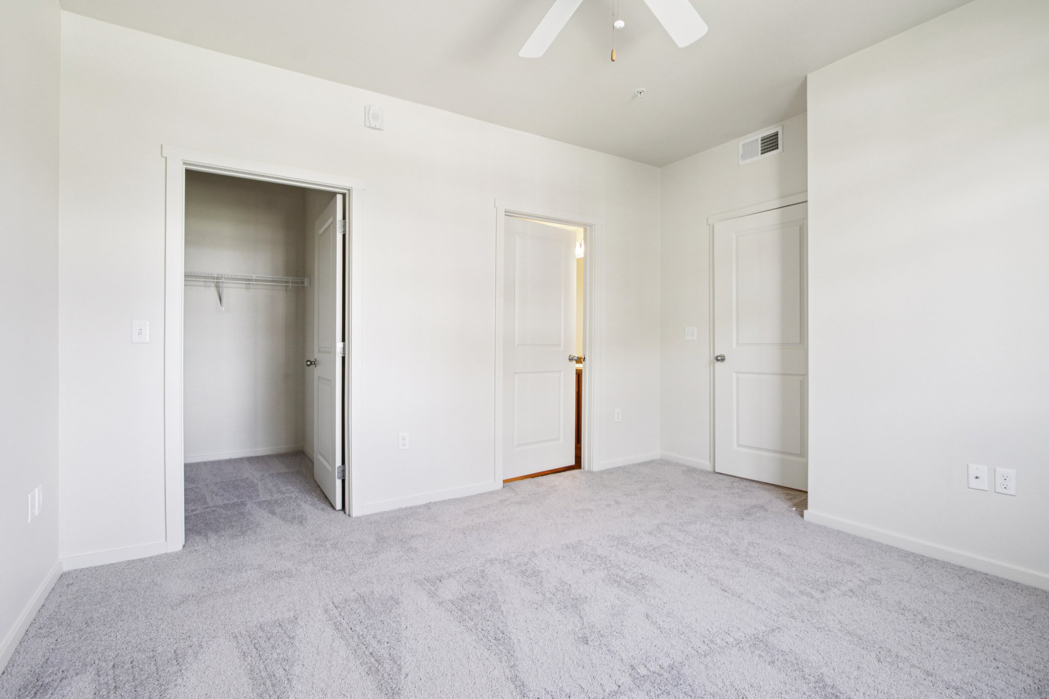 Spacious primary bedroom at Copper Peak Apartments featuring plush carpeting, ceiling fan, and walk-in closet.