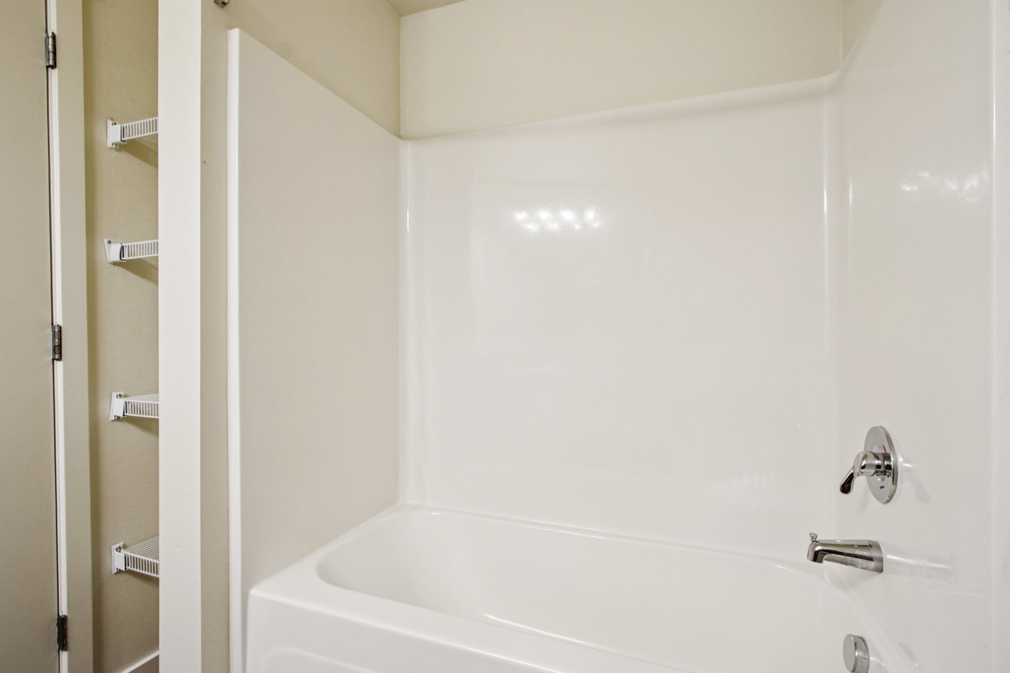 Full bathroom with tub and shower combination, linen shelving, and modern finishes at Copper Peak Apartments.