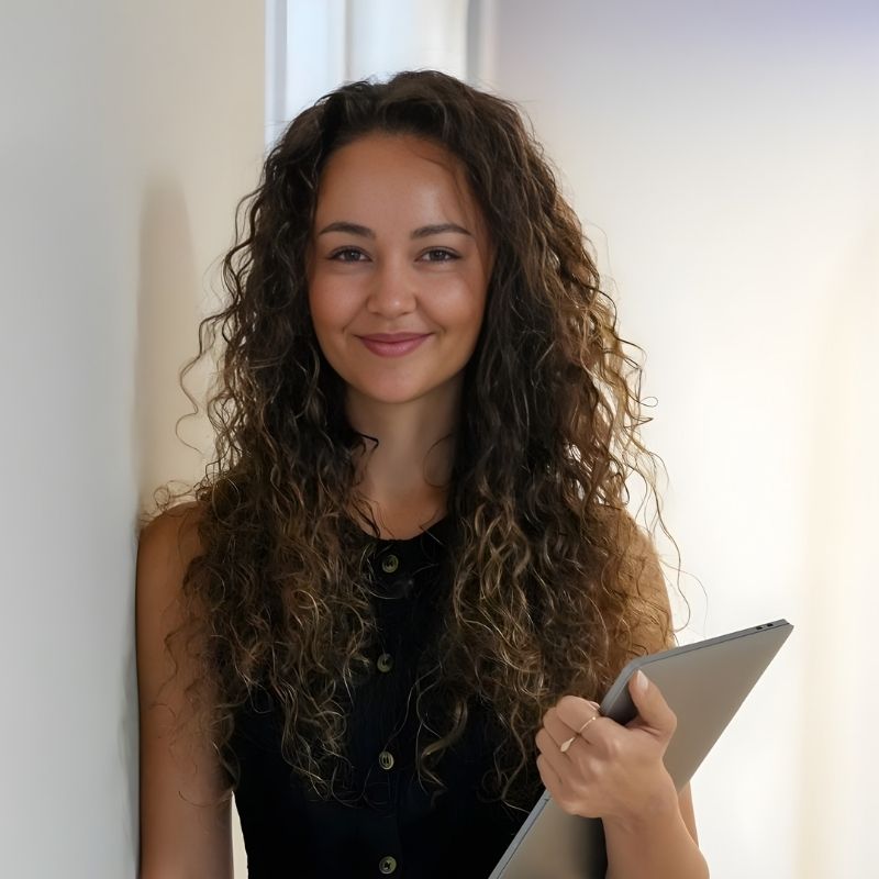 Smiling man wearing a light blue button-up shirt against a gray background.