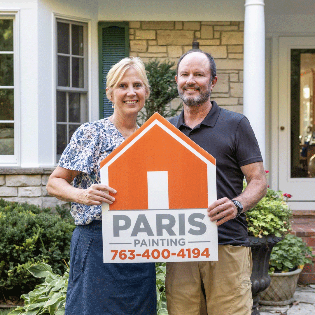 Smiling man and woman standing outside a house holding a sign that reads 'PARIS PAINTING 763-400-4194'.