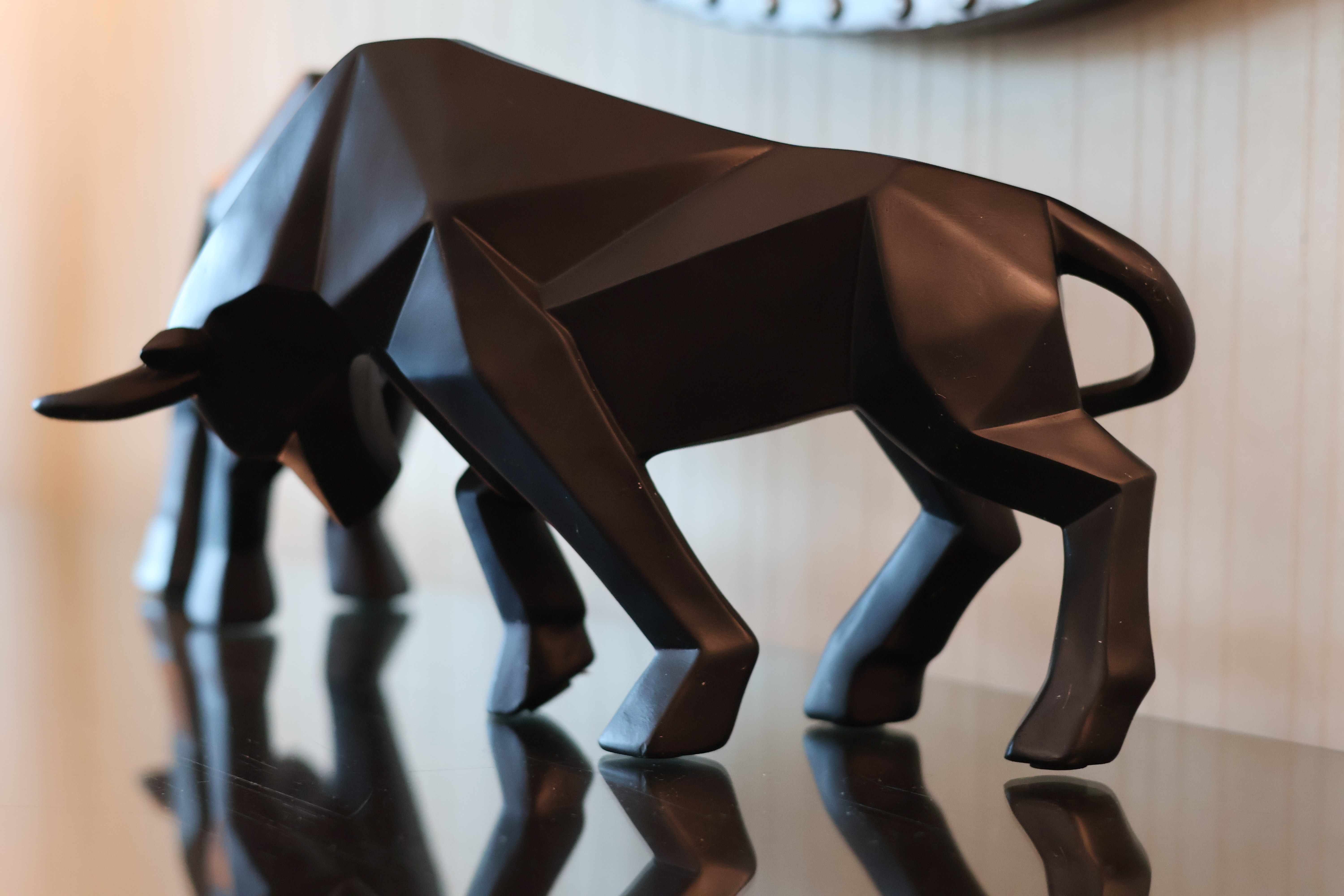 Black geometric bull sculpture on a reflective surface with a blurred background.