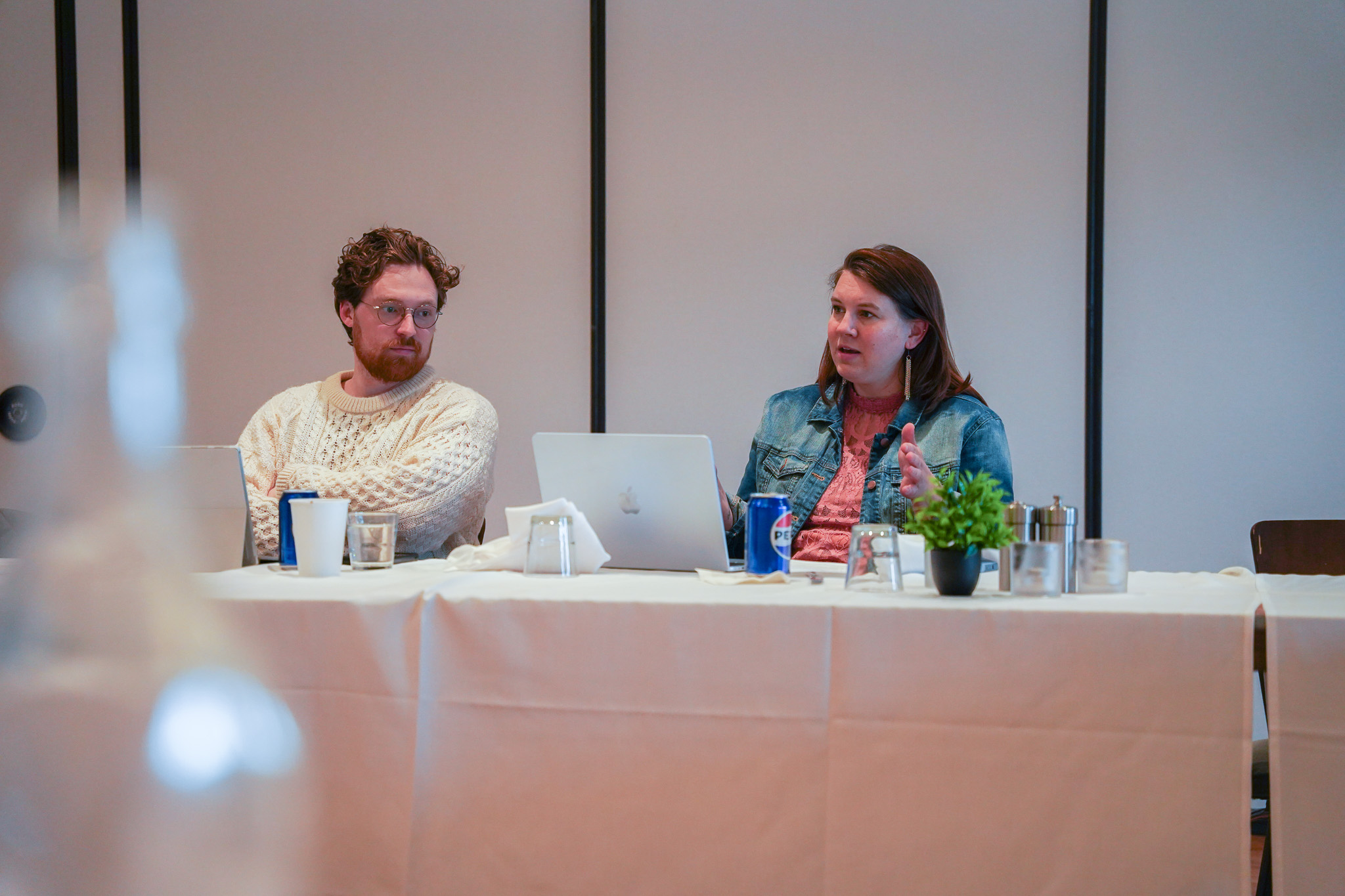 Two men working together at a desk with dual monitors, one seated and the other standing and pointing at one screen.
