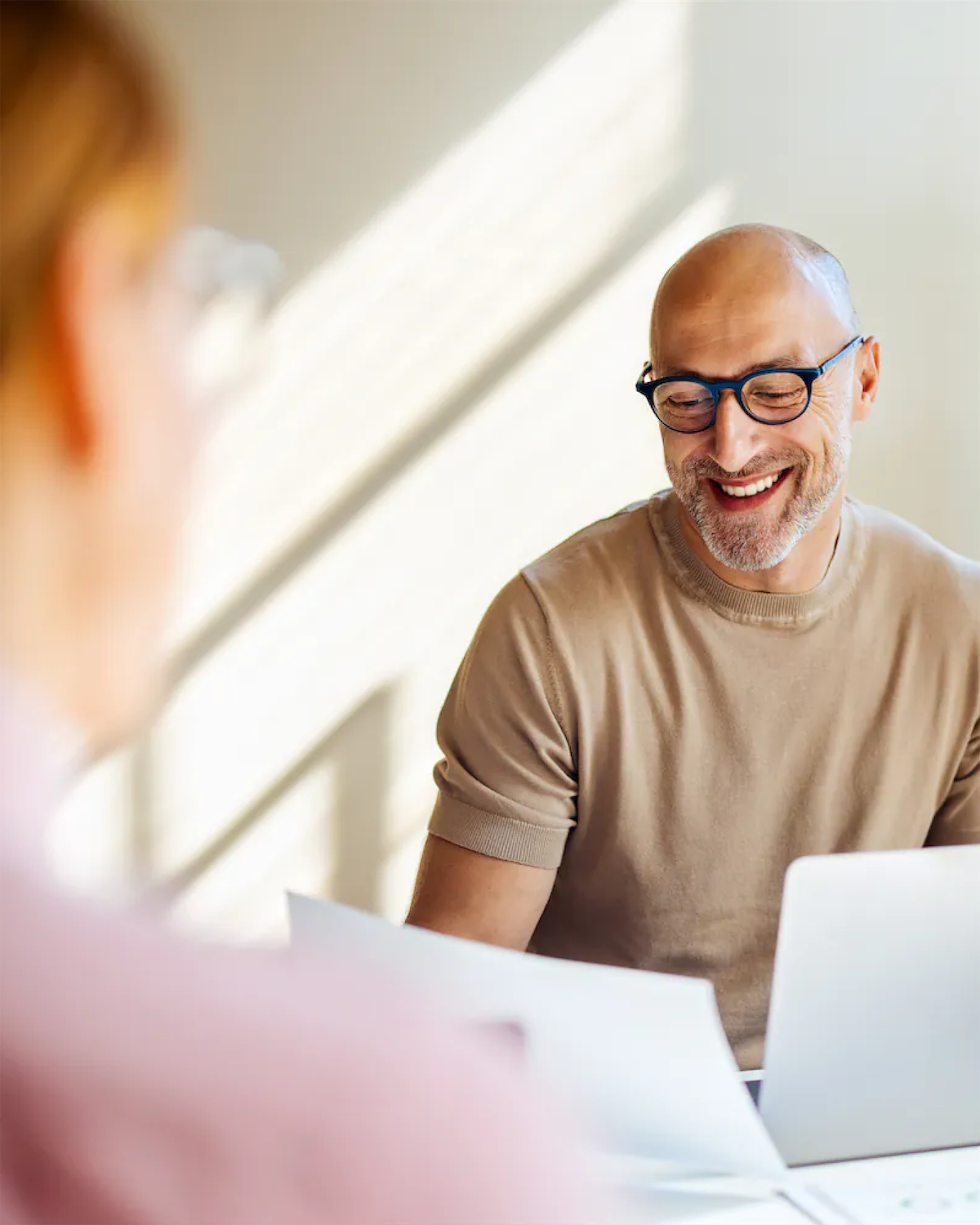Smiling bald man with glasses reviewing documents with another person at a table.