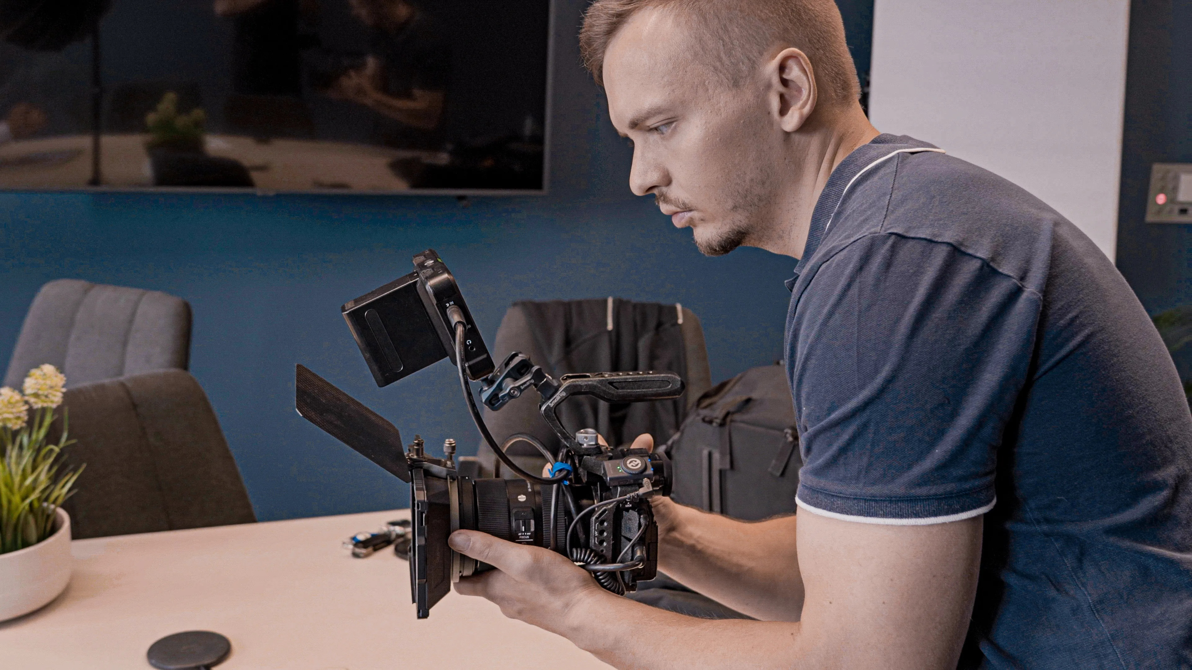 Man in a blue shirt adjusting a professional video camera on a conference room table.
