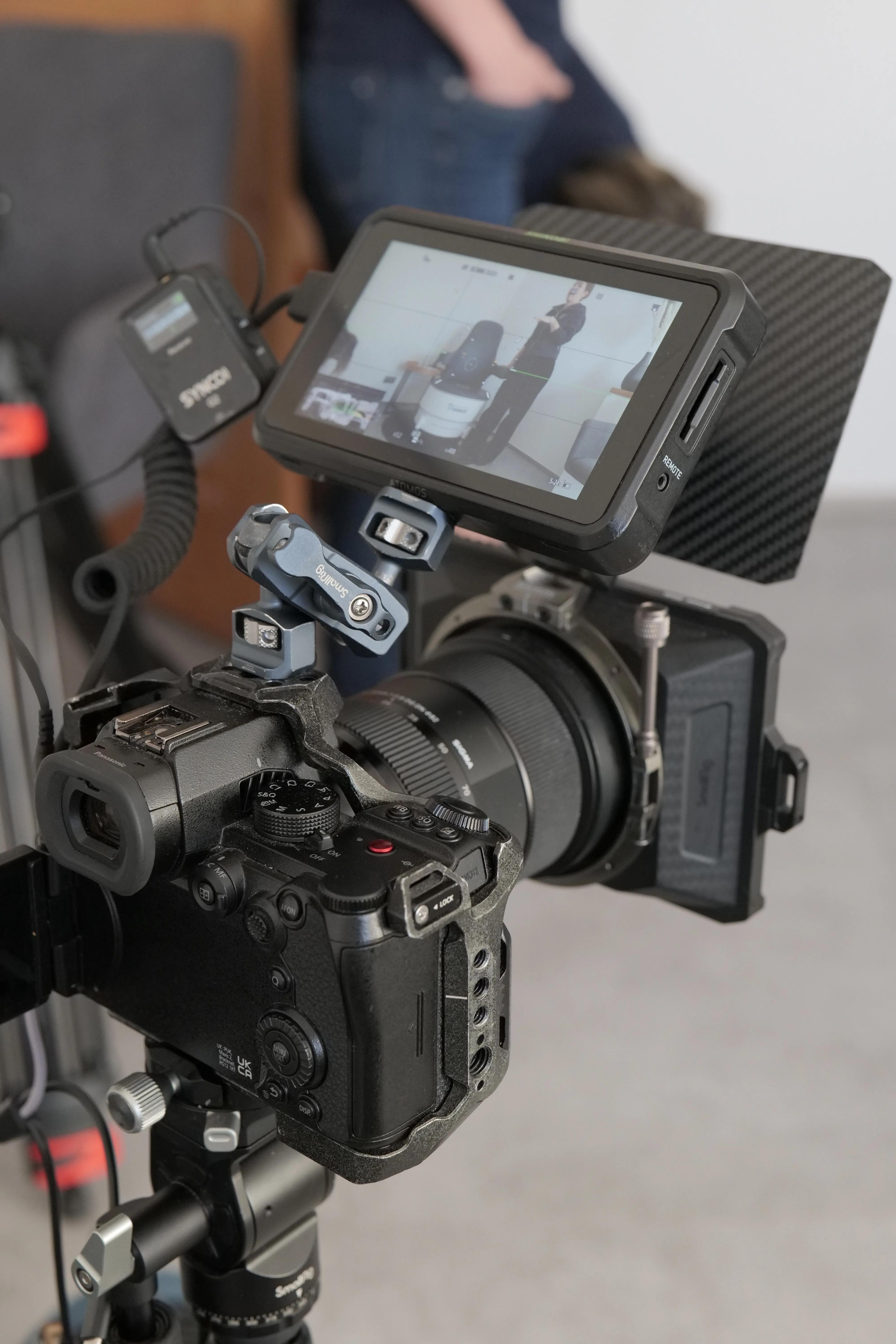 Professional video camera setup with external monitor displaying a person standing near a chair.