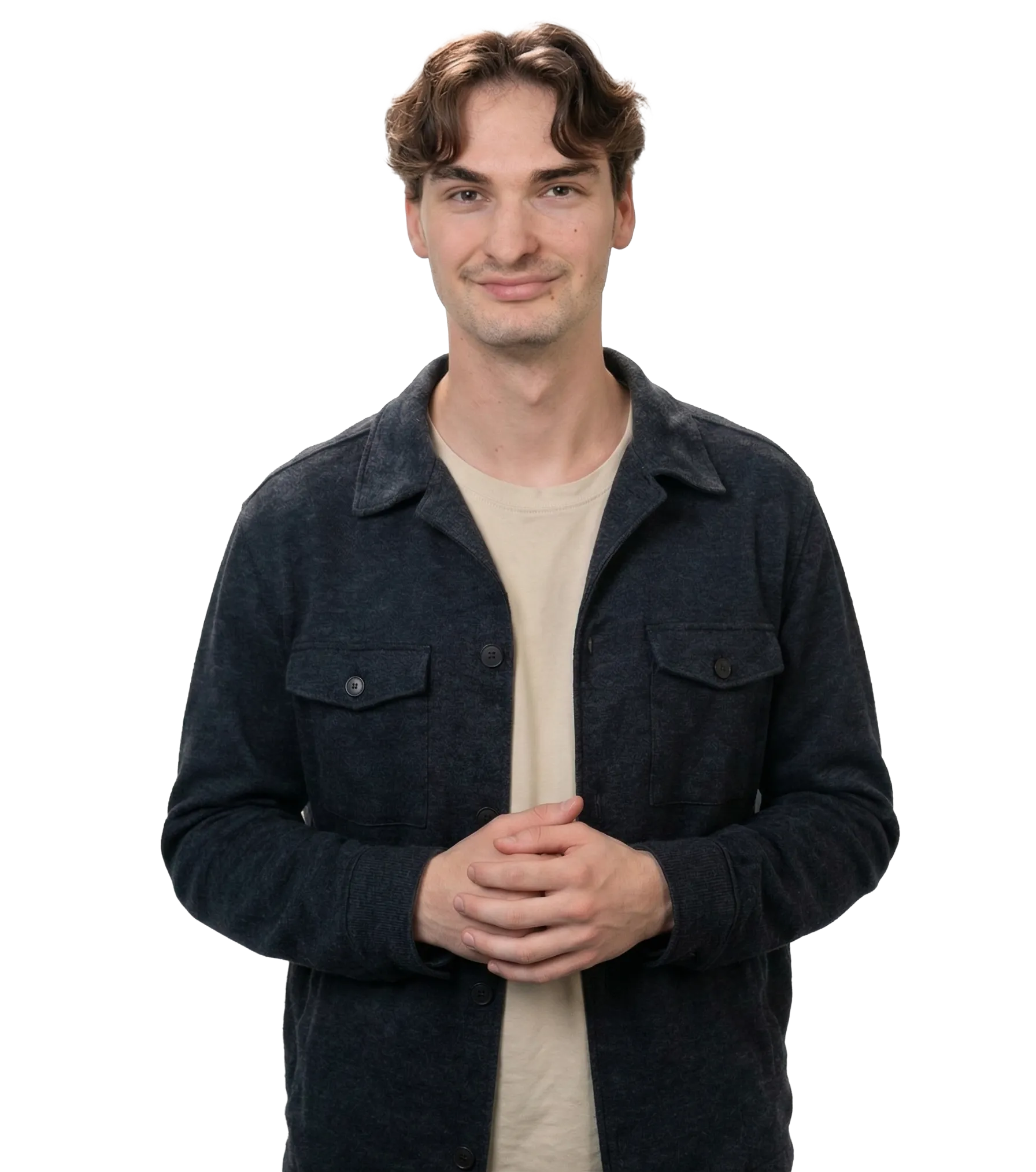 Young man with wavy brown hair wearing a beige shirt and dark buttoned jacket, smiling with hands clasped.