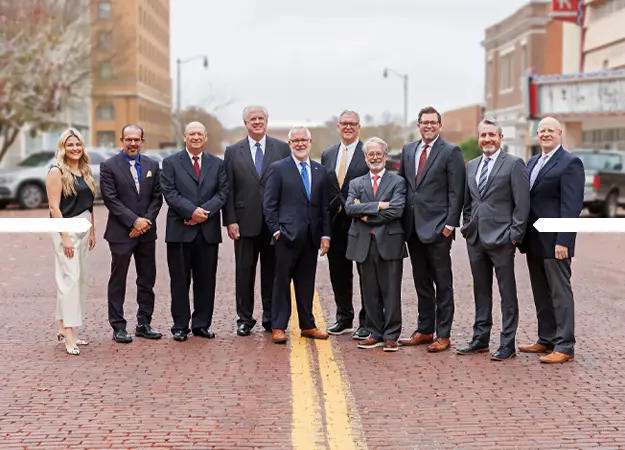 Professional group of nine men and one woman standing on a brick street with buildings in the background.