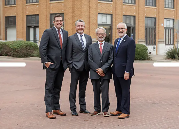 Four men in business suits standing outside a brick building, smiling at the camera.