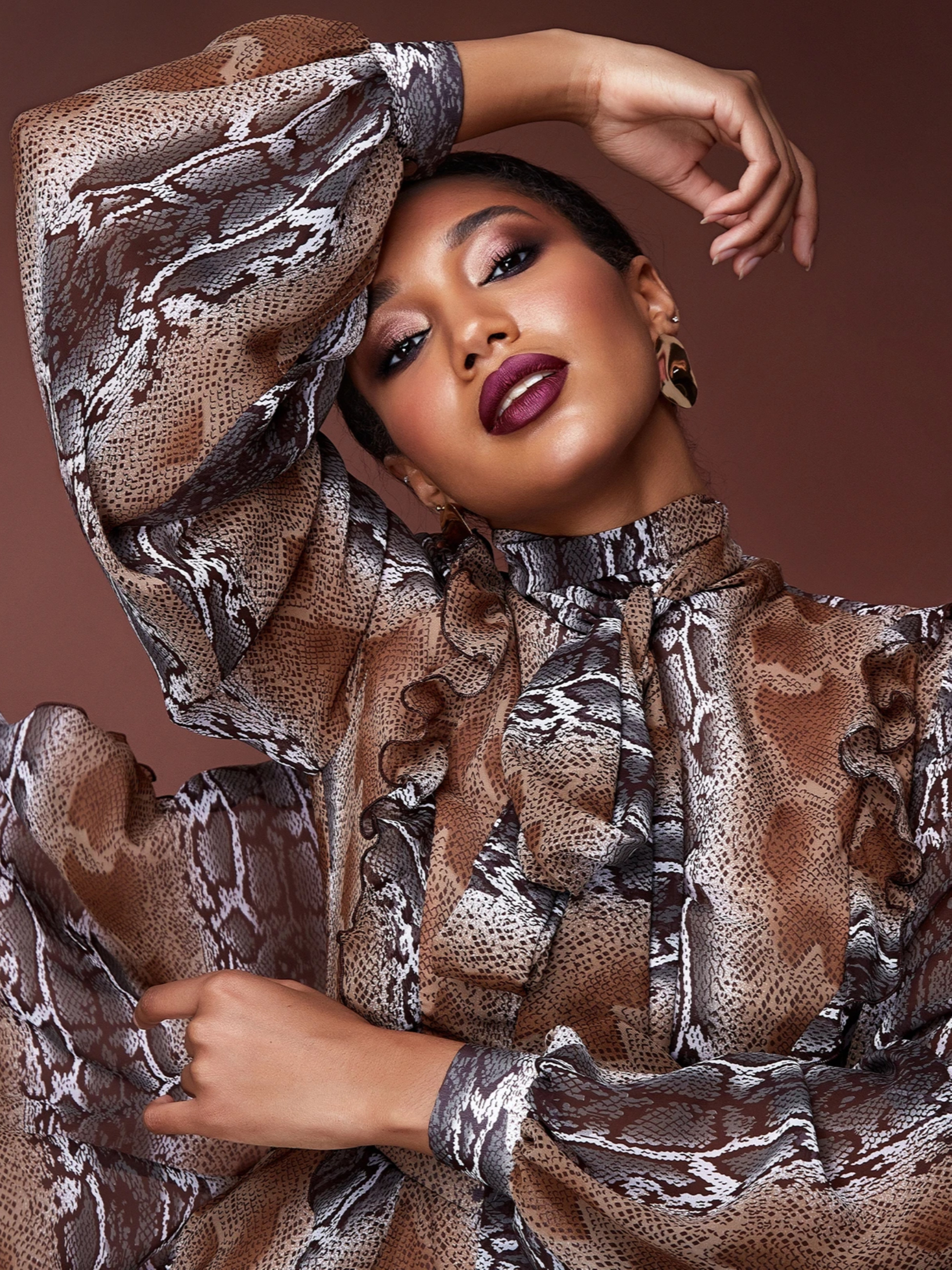 Close-up of a woman wearing a sheer snake-print blouse with ruffles, posing with one arm raised.
