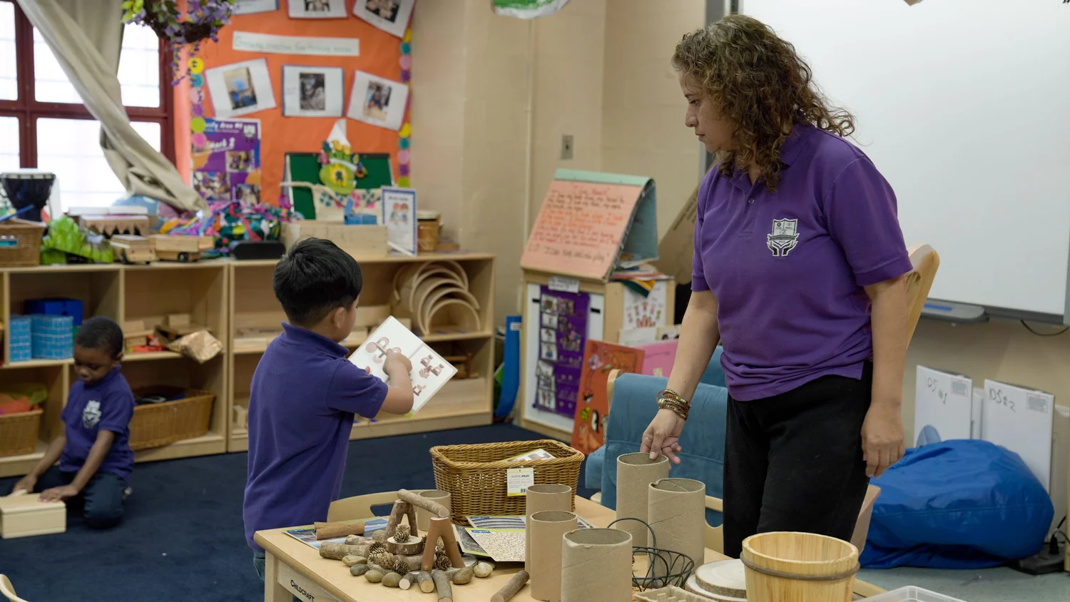 A teacher attentively helps a young boy 