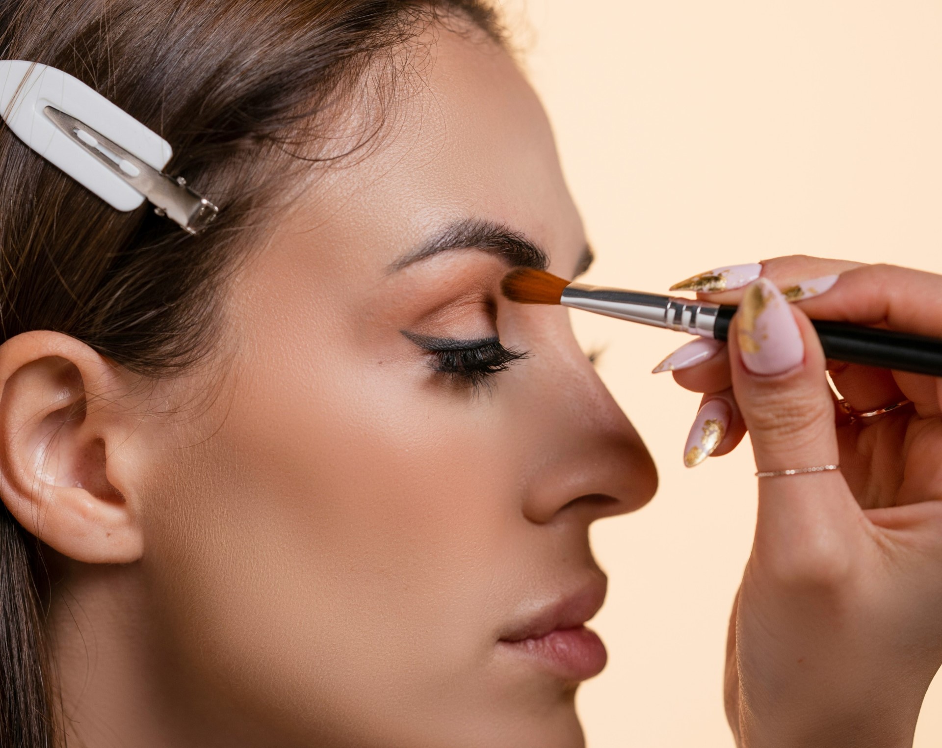 Professional stylist applying makeup and styling hair with brush tool