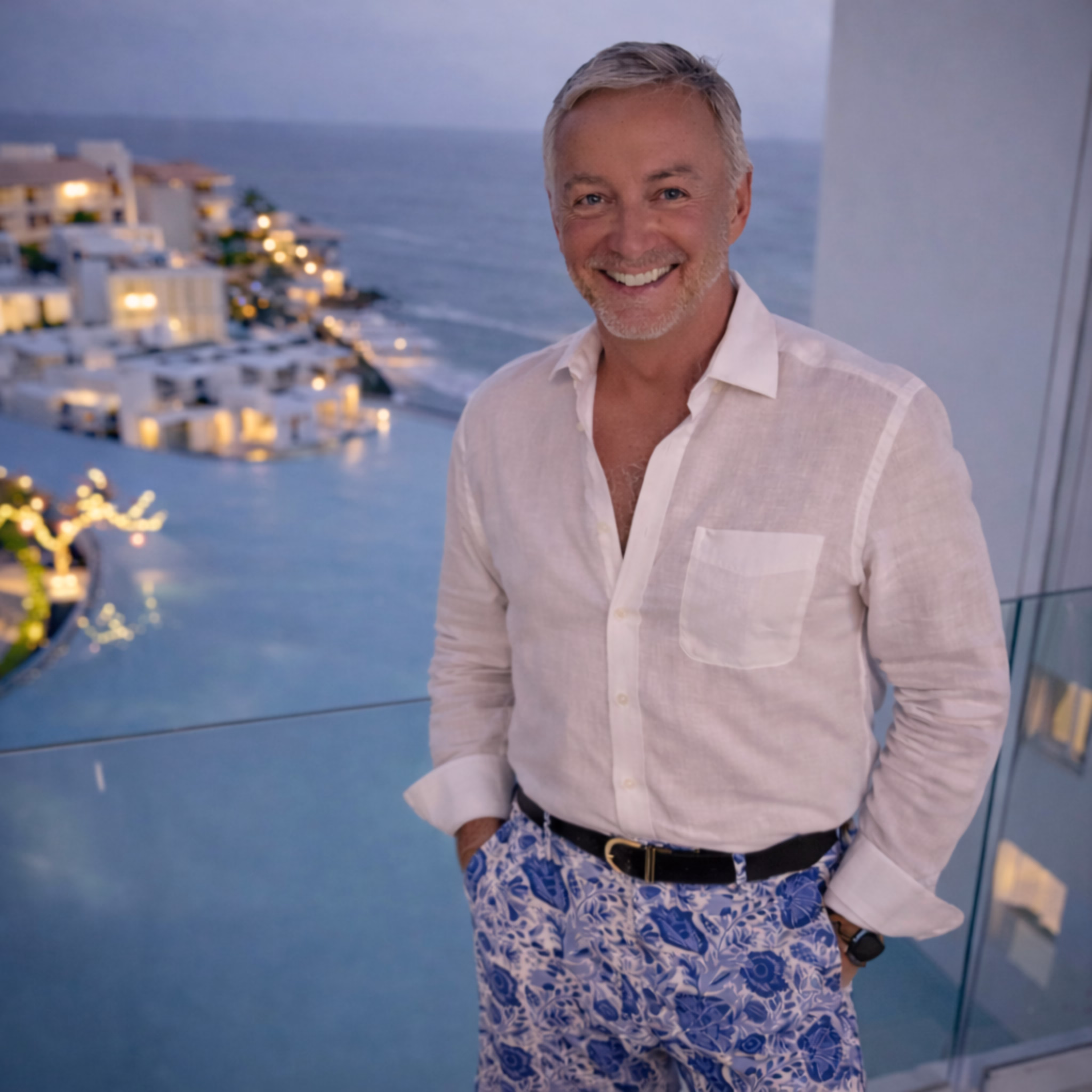 Smiling middle-aged man in gray shirt and black shorts holding a tennis racket on his shoulder and a tennis ball in hand.
