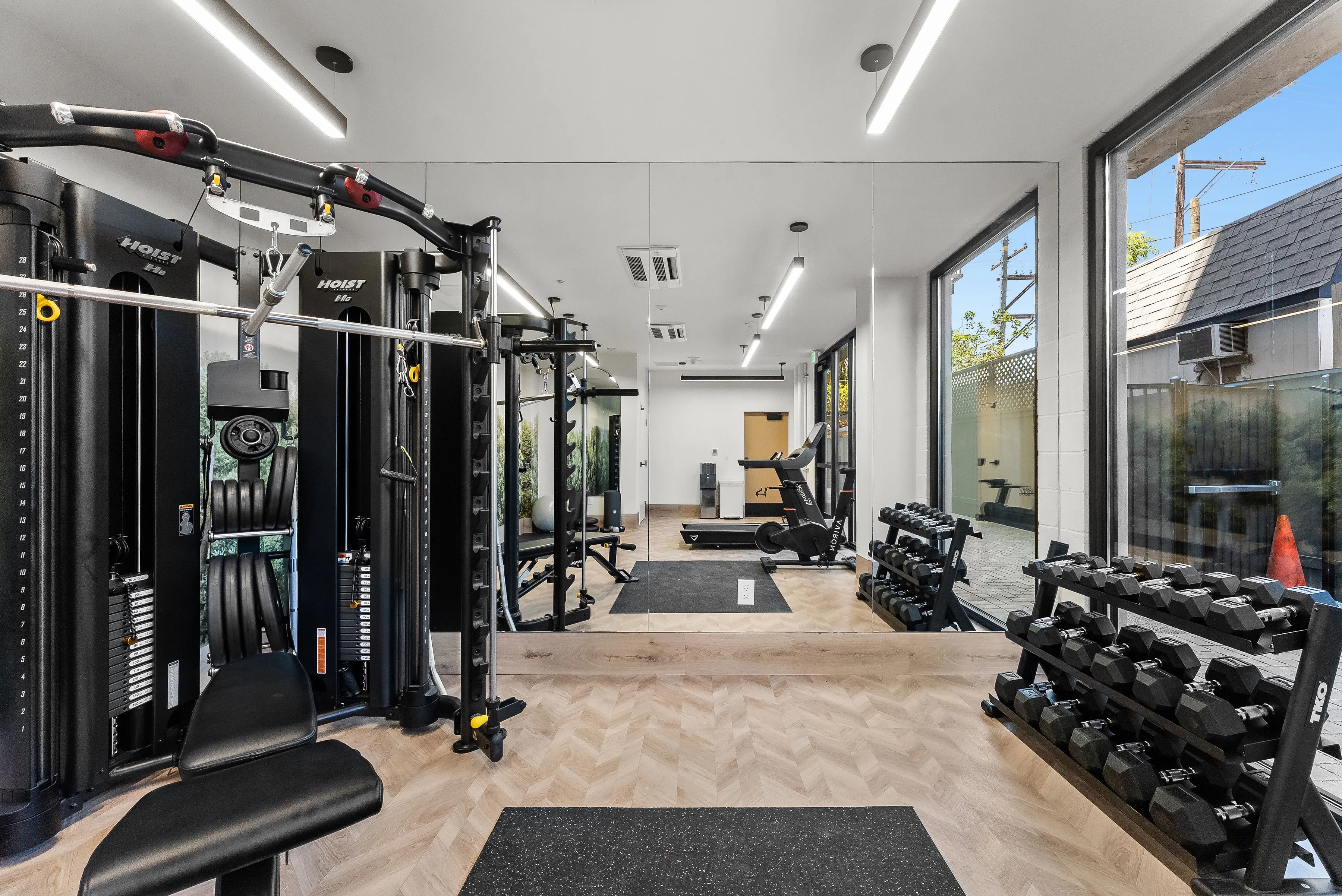 Bright gym with weight machine, dumbbell rack, treadmill, exercise bike, and large mirrors.