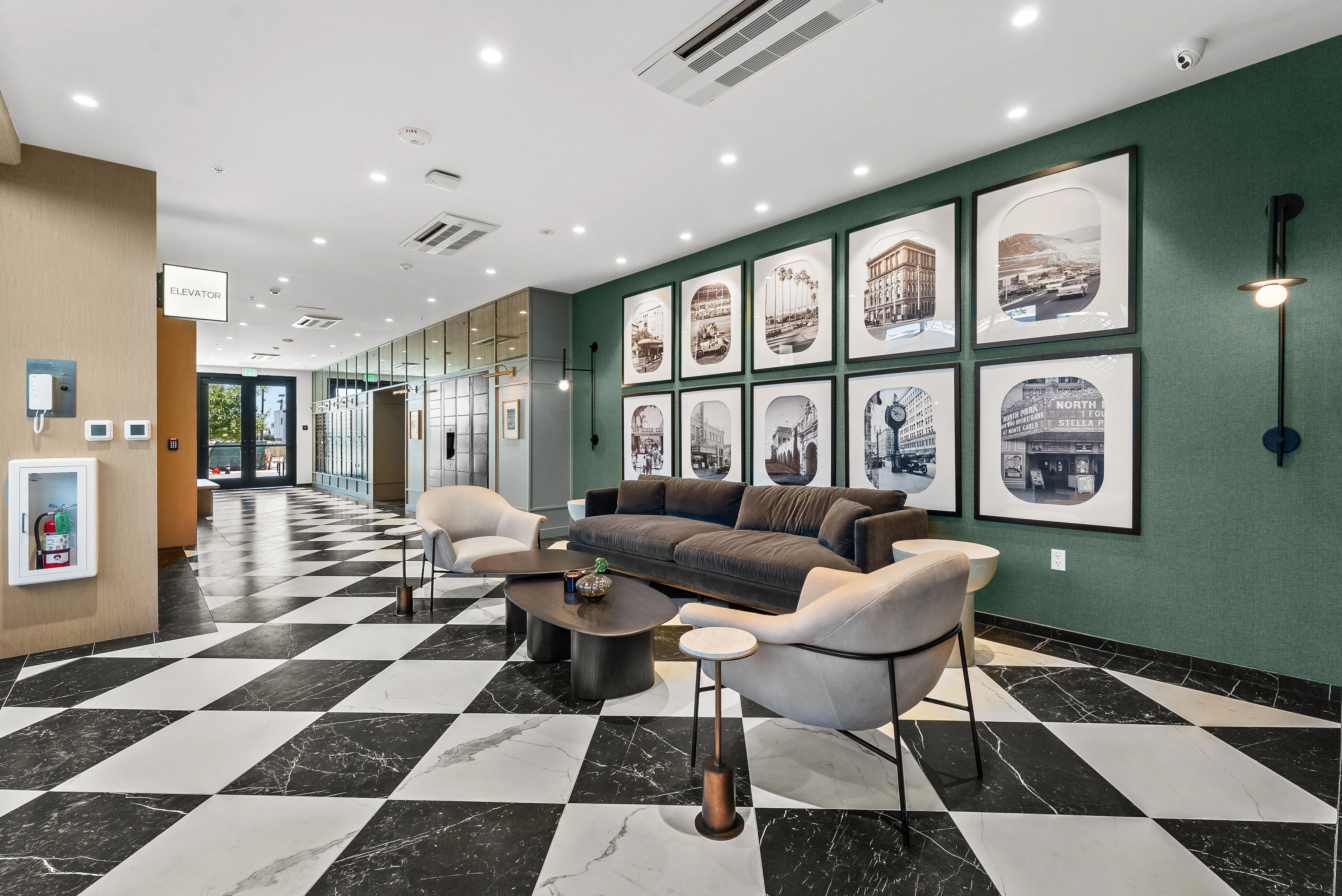 Modern lobby with black and white checkered floor, gray sofa, armchairs, and framed black-and-white photos on wall.