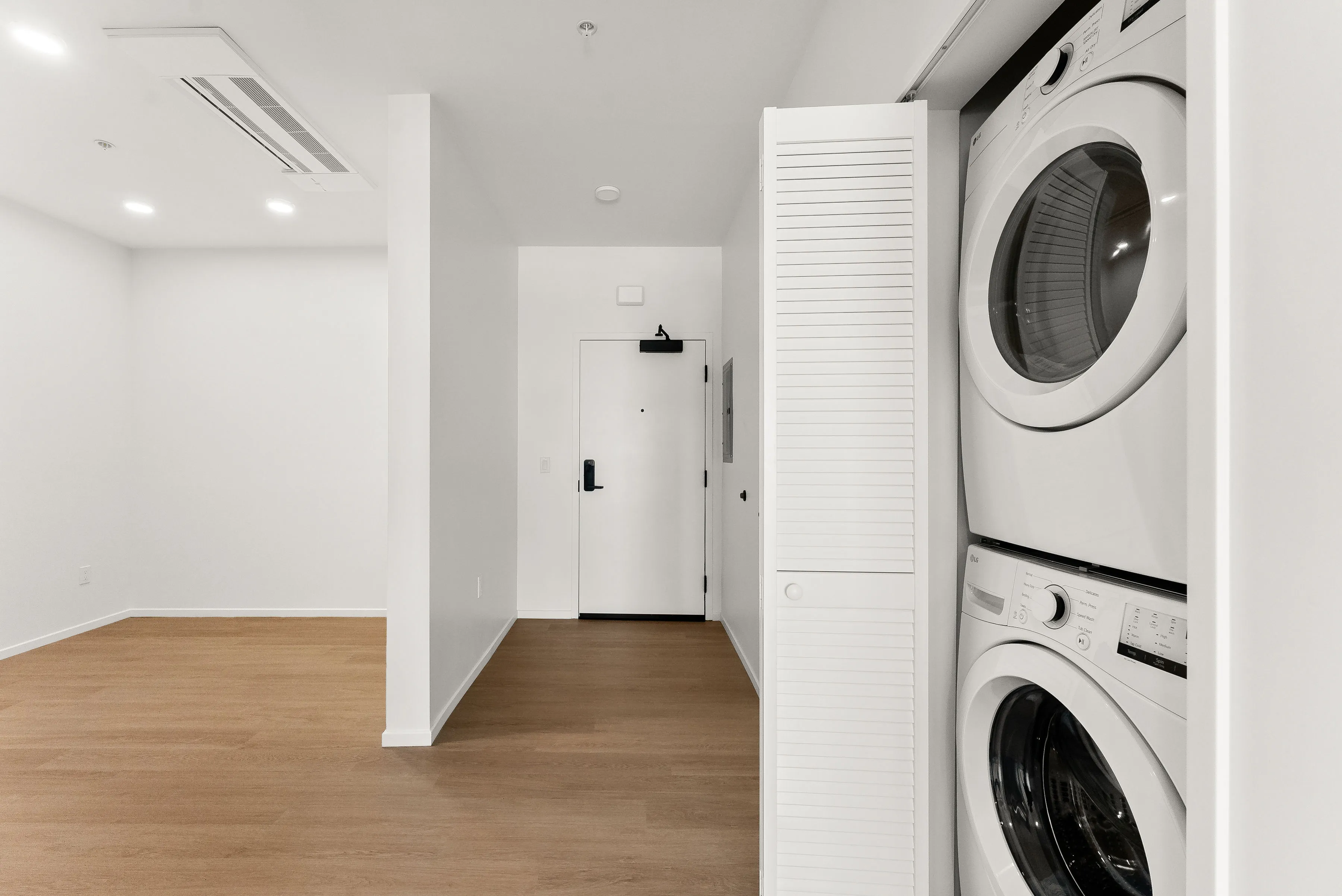 Modern laundry area with stacked washer and dryer in a bright room with white walls and wood flooring.