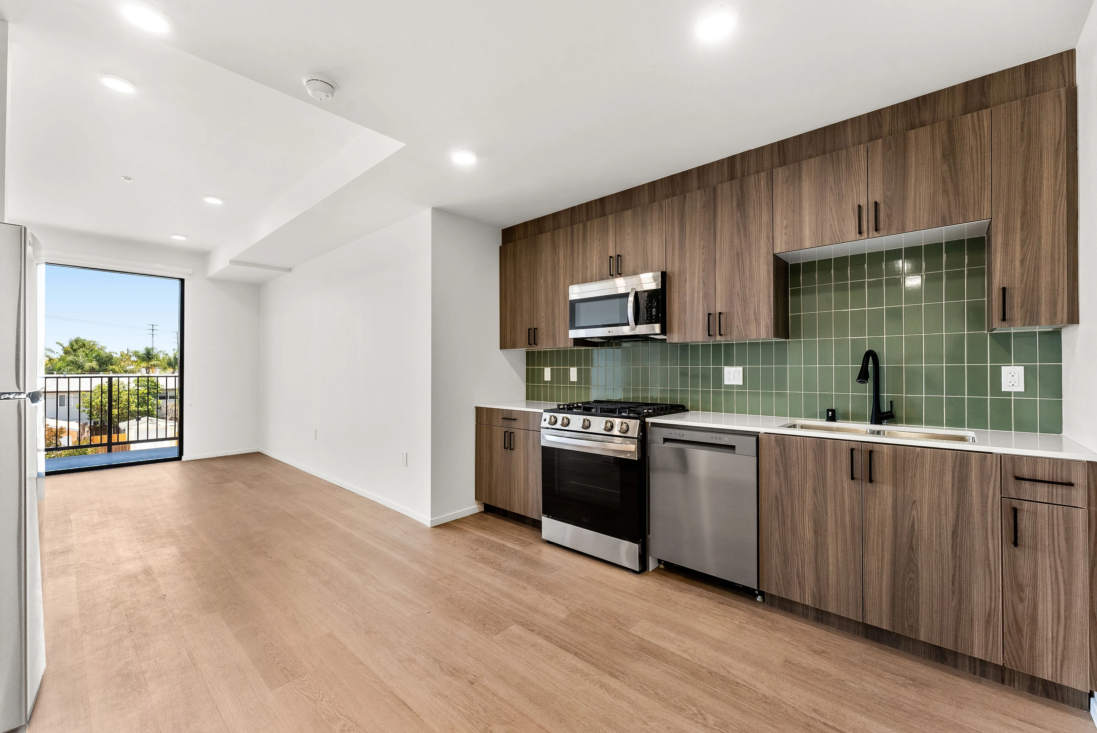 Modern kitchen with wood cabinets, green tile backsplash, stainless steel appliances, and light hardwood floor.
