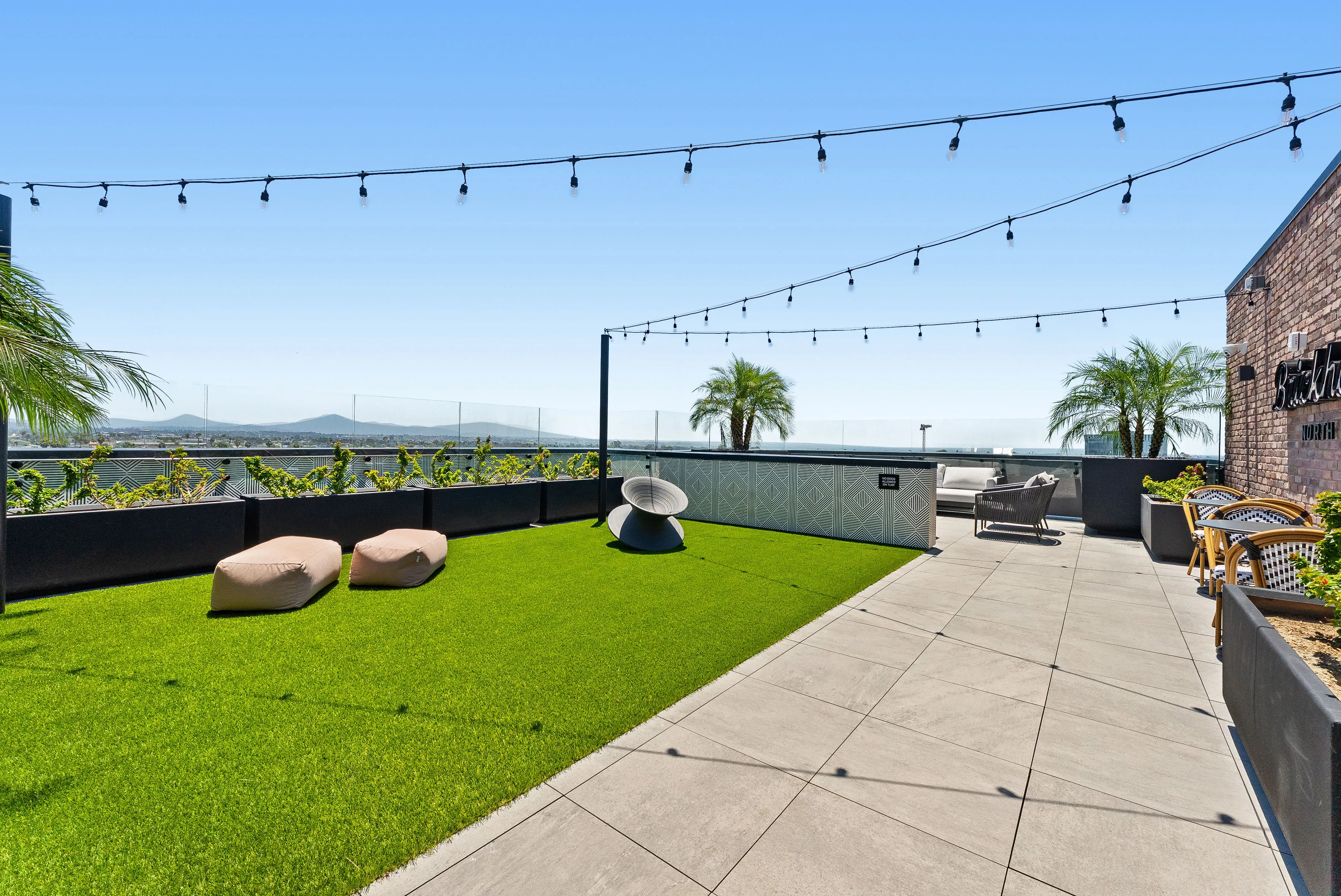 Rooftop patio with green artificial grass, outdoor chairs, string lights, and a city view.