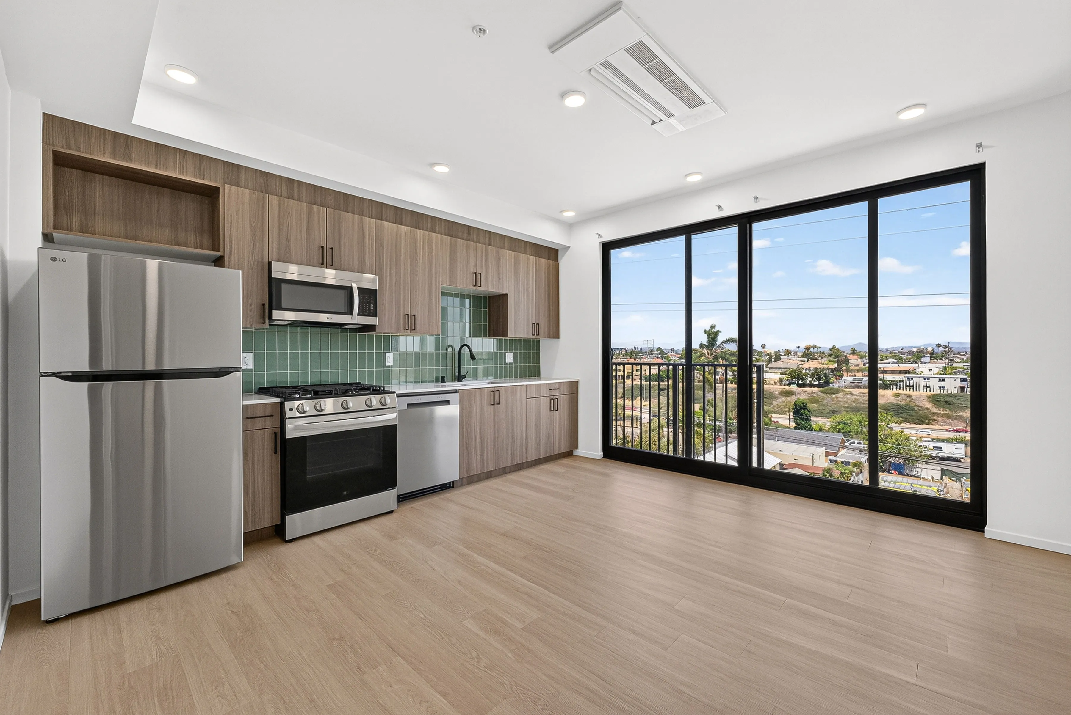 Modern kitchen with stainless steel appliances, wood cabinets, green tile backsplash, and large sliding glass doors.