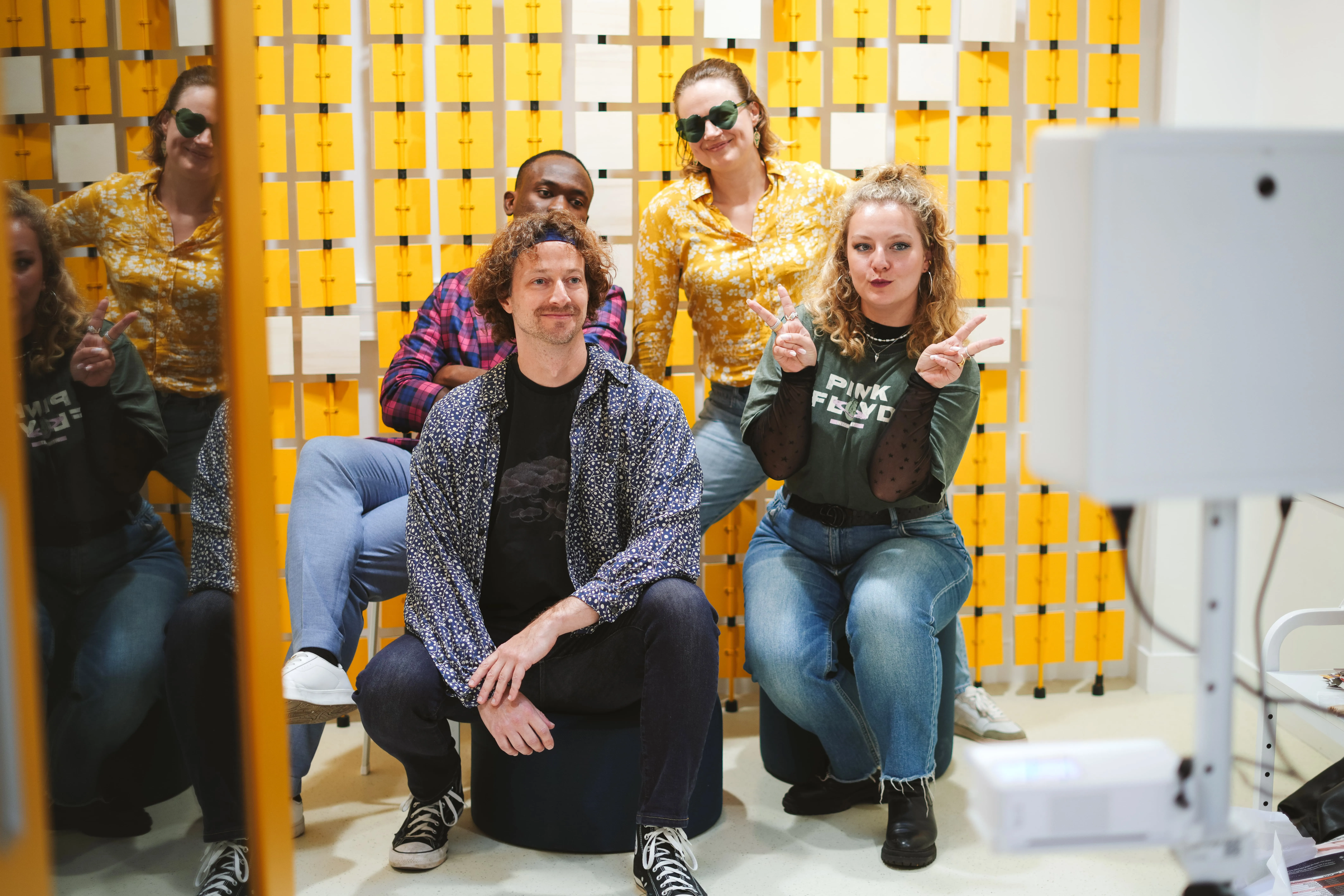 Three people sitting on colorful modern couches in a brightly lit room with turquoise walls and circular blue wall decorations, using laptops.