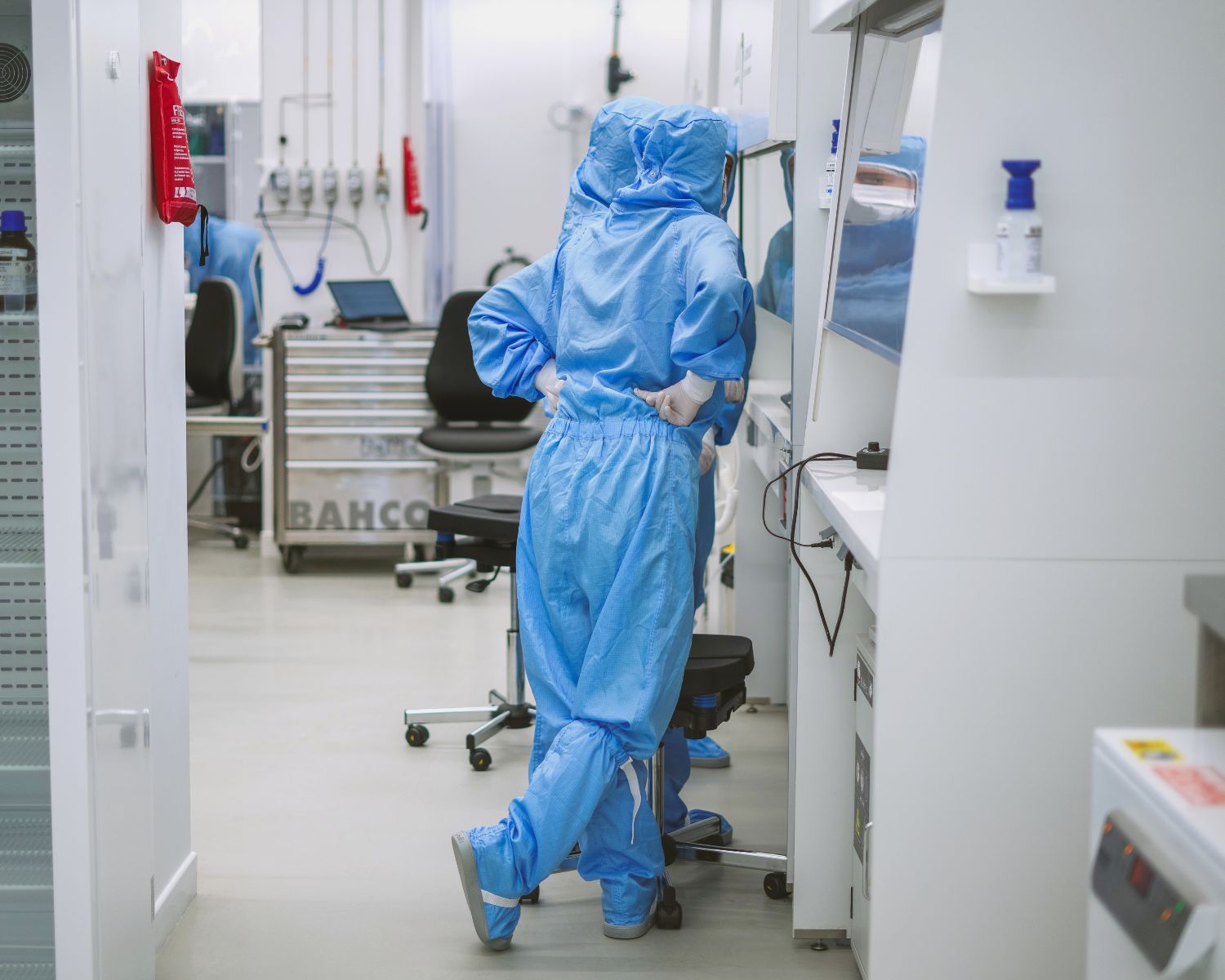 Three people sitting on colorful modern couches in a brightly lit room with turquoise walls and circular blue wall decorations, using laptops.