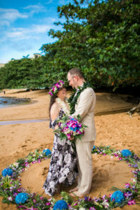 Husband and wife in a flower circle on the beach in Kauai.