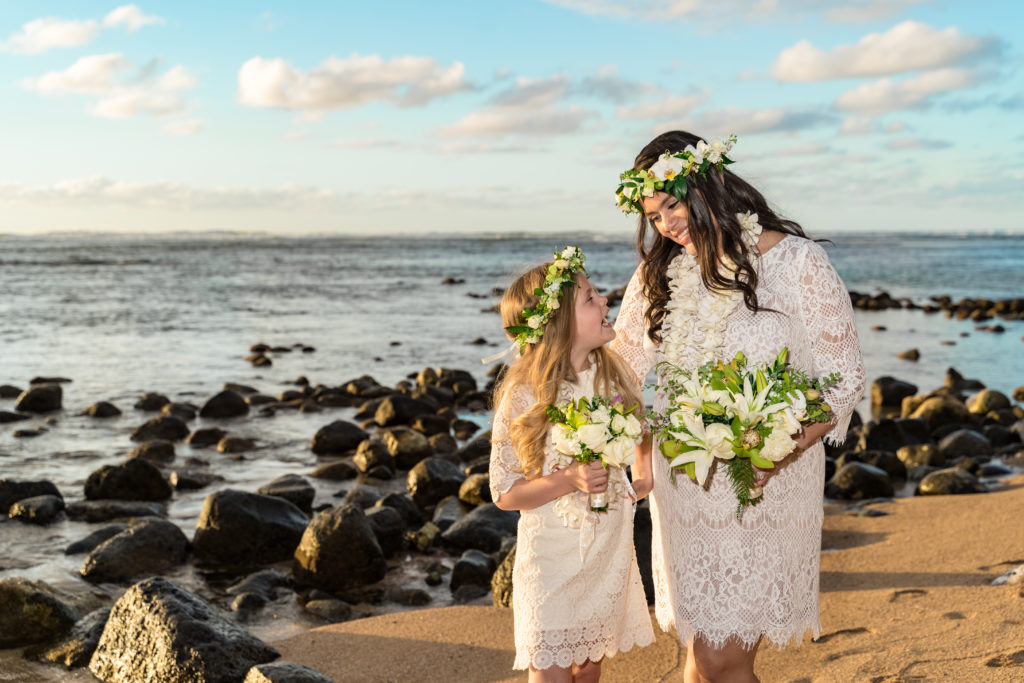Bride and daughter on the beach holding flowers.