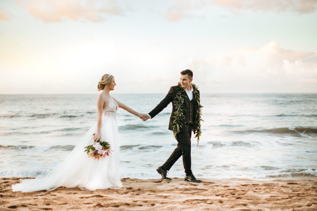 Bride and groom walk on the beach.