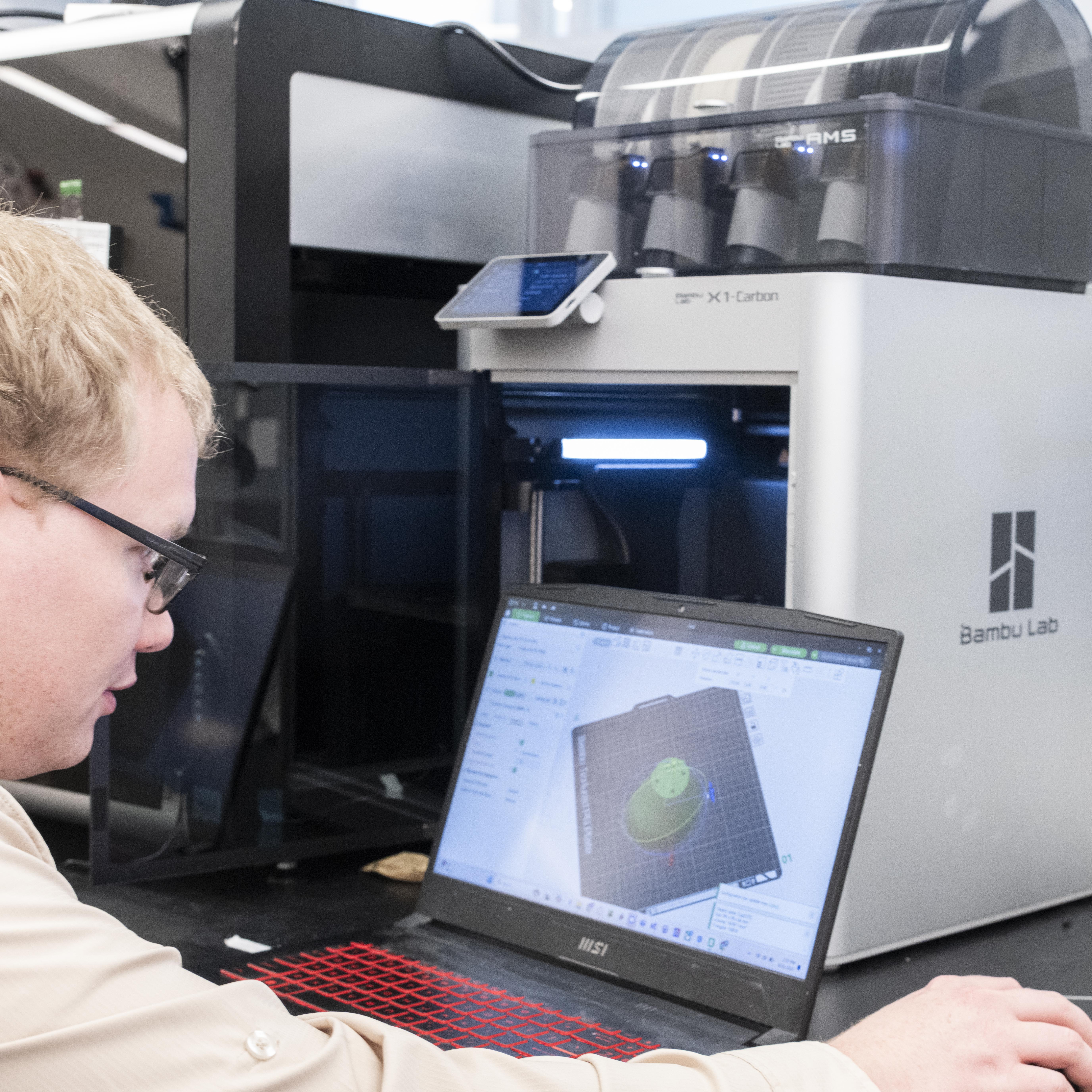 PDTI engineer sending an STL file from a laptop with 3D modeling software displayed to a Bambu Lab X1-Carbon 3D printer.