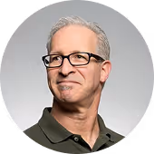 Middle-aged man with gray hair and glasses wearing a dark green collared shirt, looking slightly to his left.