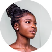 Portrait of a young Black woman with braided hair styled in an updo, looking slightly upward and to the side against a plain light background.