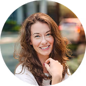 Smiling woman with curly brown hair outdoors in a blurred urban background.