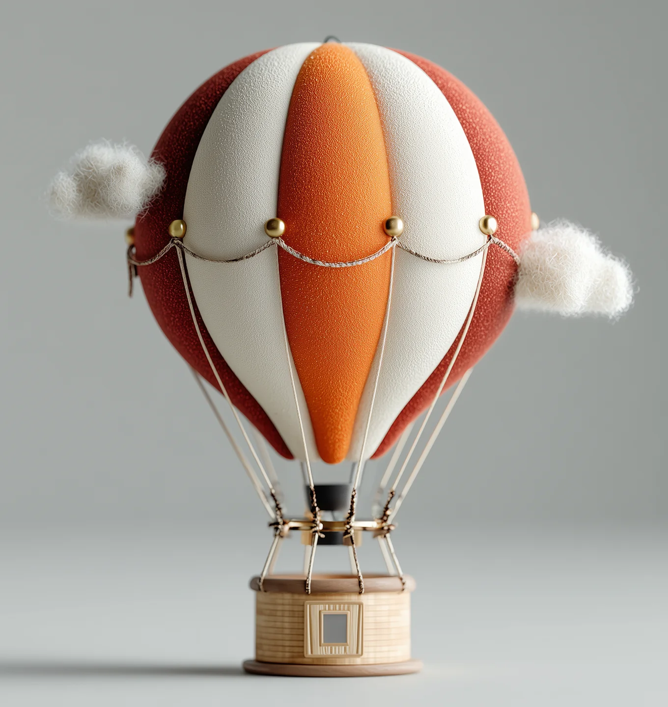 Miniature hot air balloon model with orange, white, and red panels, attached to a wooden basket and surrounded by small fluffy clouds.