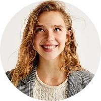 Smiling woman with light brown hair wearing a knitted cream sweater and checkered blazer.