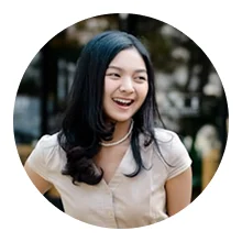 Young woman with long black hair smiling and looking to the side outdoors.