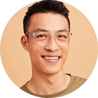 Young man with short black hair and clear glasses smiling against a beige background.