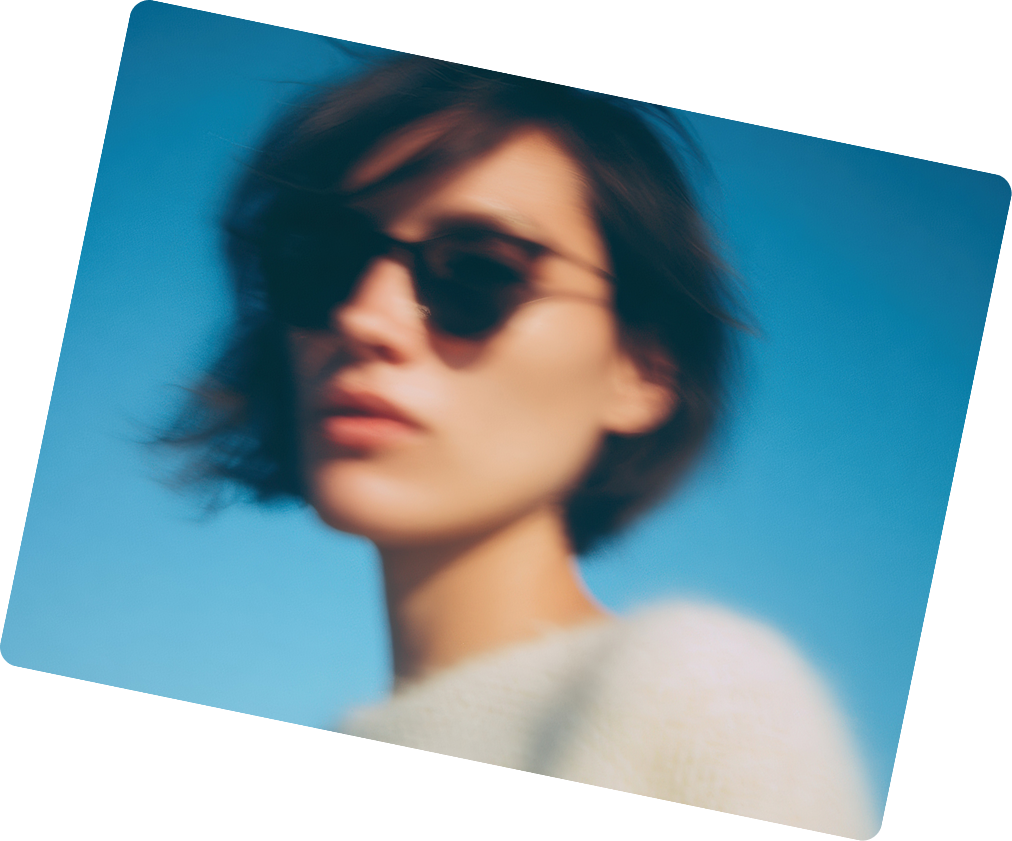 Blurred portrait of a person with short hair wearing dark sunglasses against a blue sky.