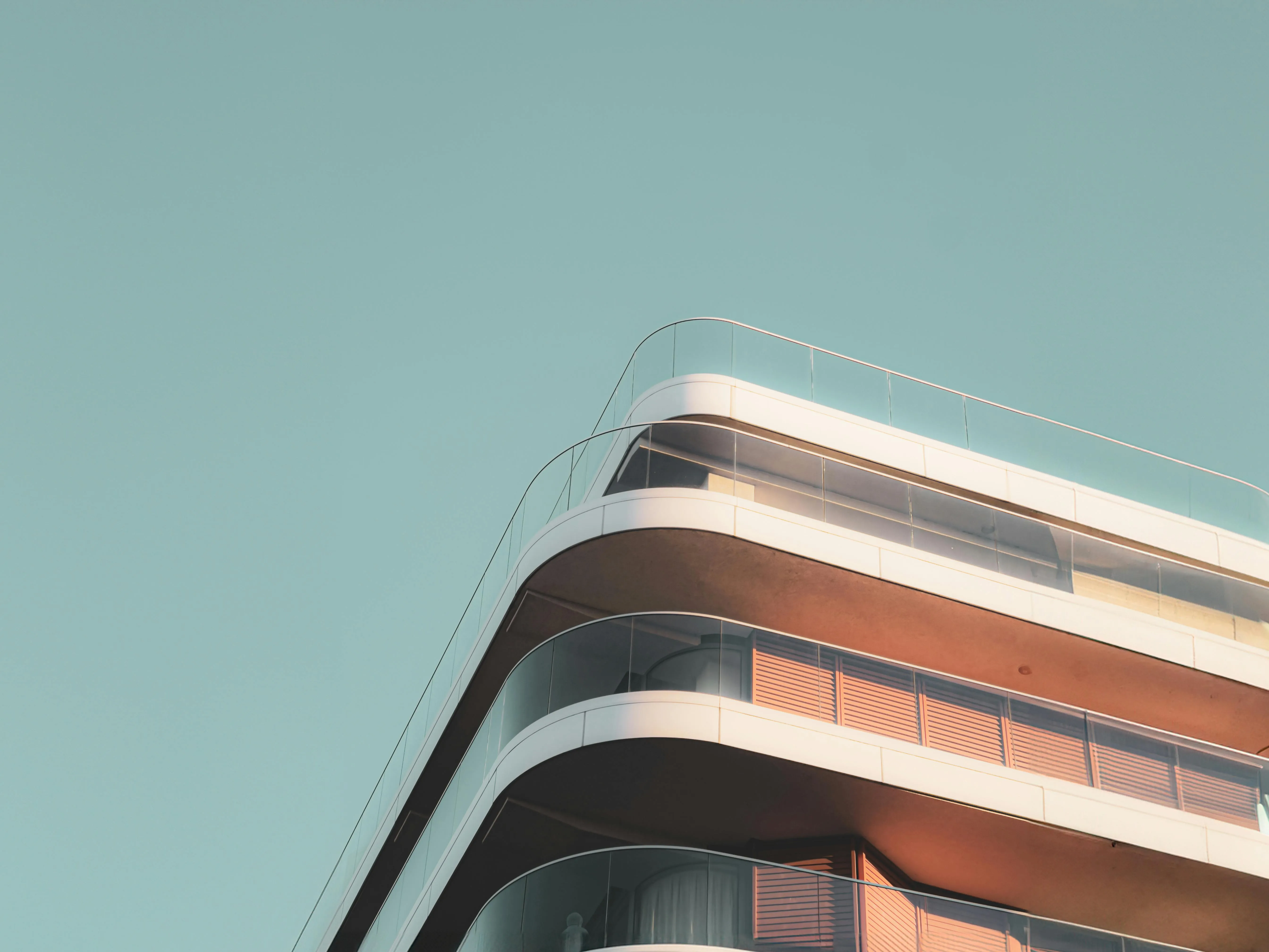 Corner view of a modern building with rounded balconies and glass railings under a clear blue sky.