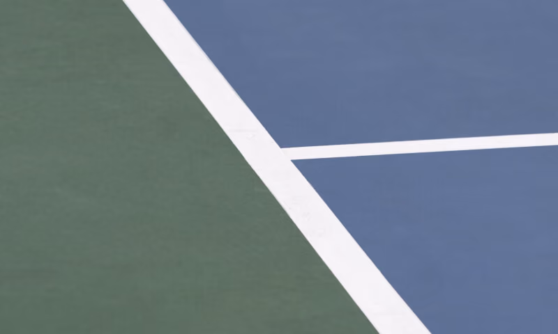 Close-up of a tennis court corner with green and blue surfaces divided by white lines.