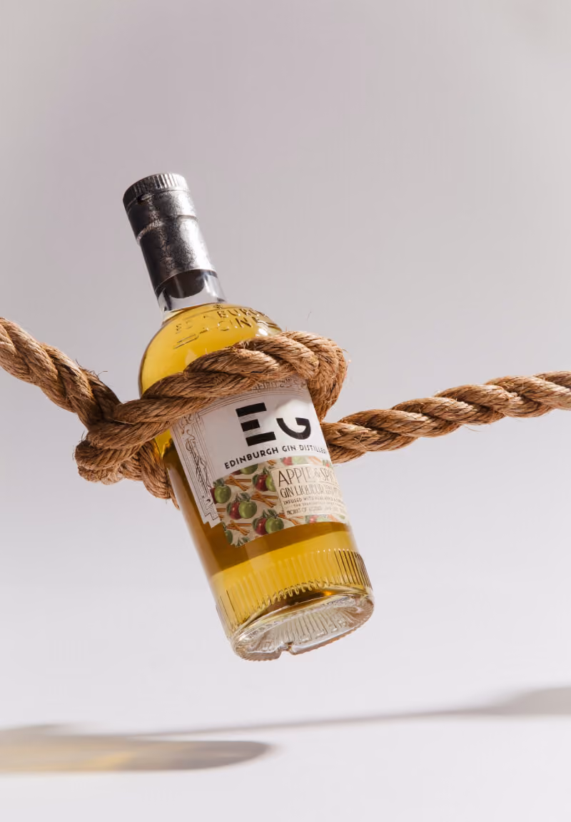 Bottle of Edinburgh Gin Apple & Spice wrapped in a thick brown rope against a plain background.