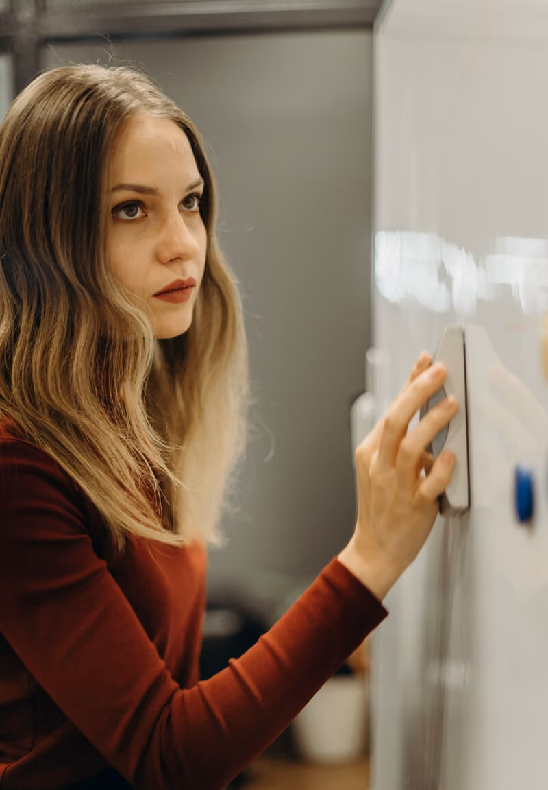 Young woman in red sweater erasing a whiteboard with an eraser in an office setting.