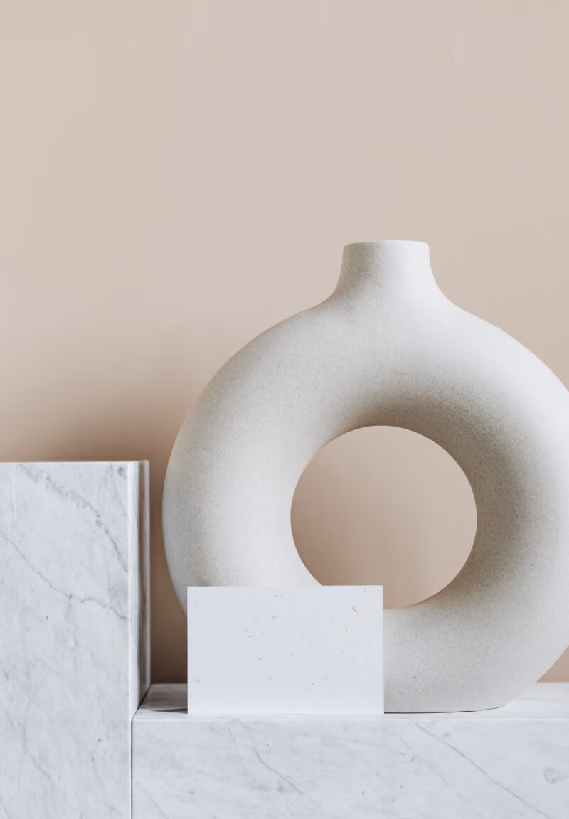 White circular ceramic vase with a hollow center on marble block with blank white card in front.