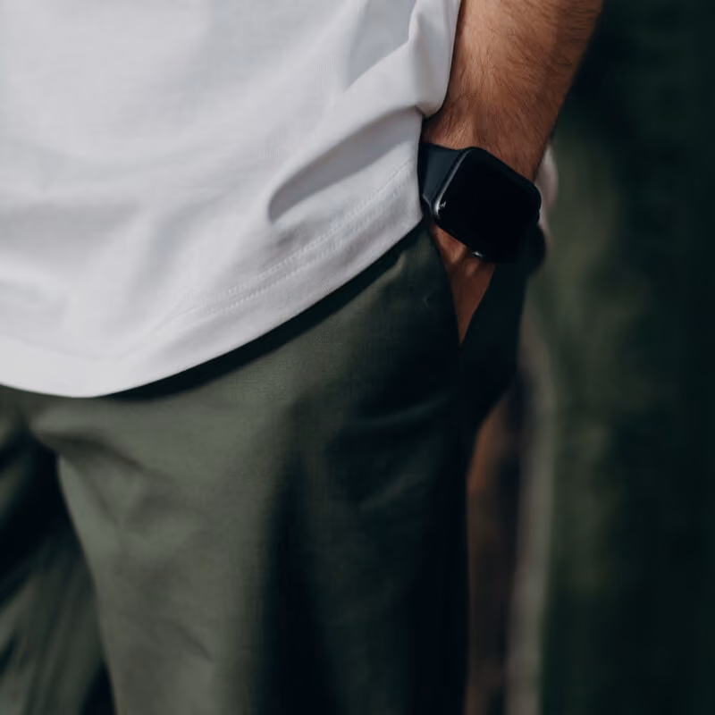 Person wearing a white shirt and green pants with a black smartwatch on their wrist.