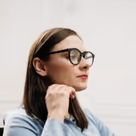 Profile of a woman with glasses looking forward, resting her chin on her hand.