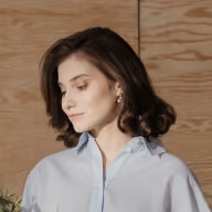 Woman with short brown hair wearing a light blue shirt looking down and to the side.