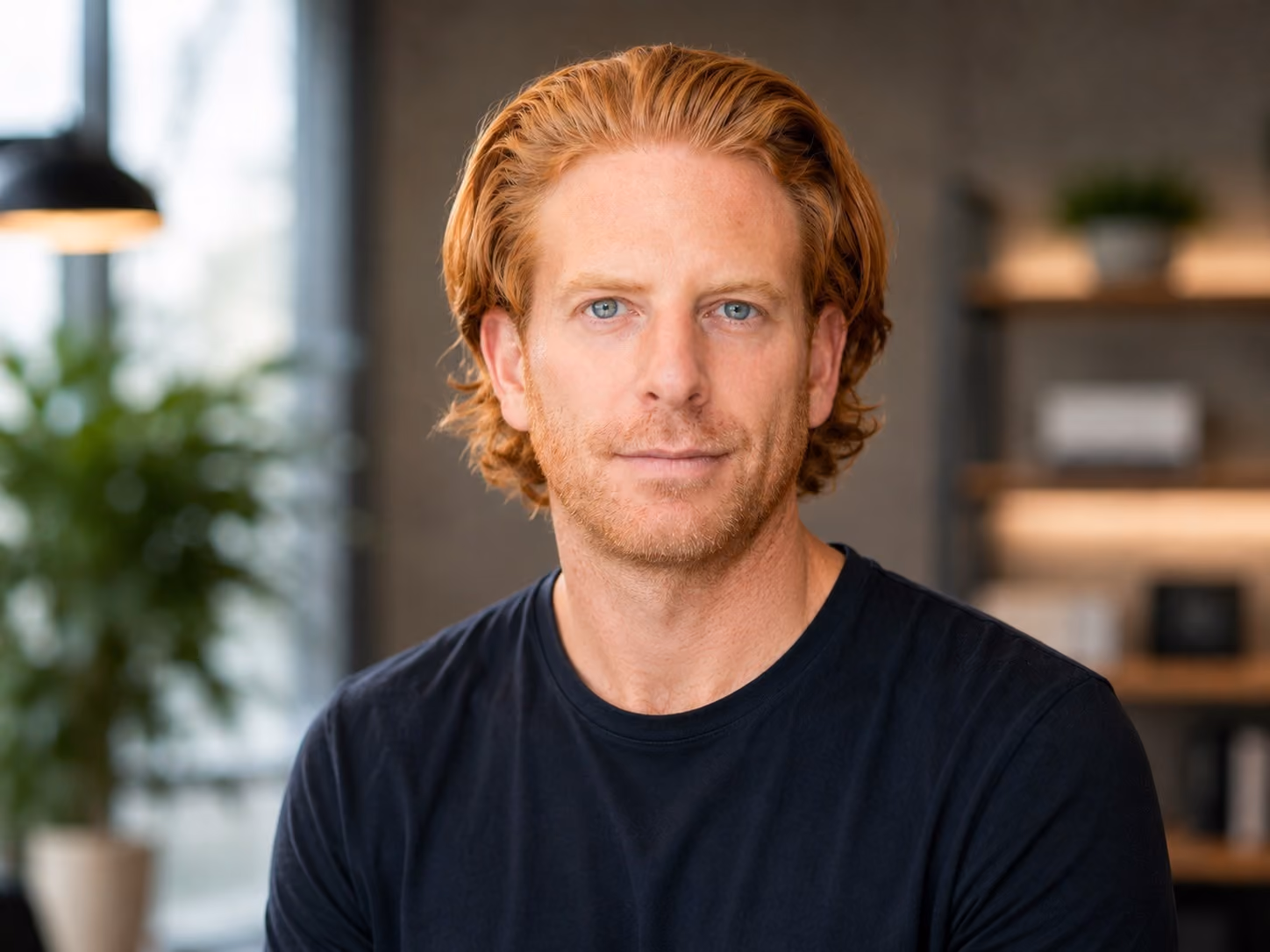Portrait of a man with red hair and blue eyes wearing a black shirt in a modern indoor setting.