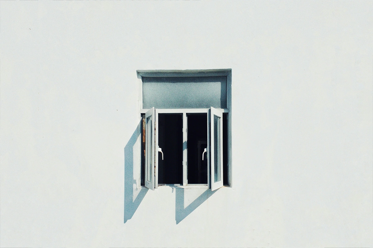 Open white window with two panes casting distinct shadows on a plain white wall.