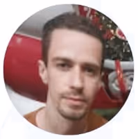 Young man with short brown hair wearing a dark shirt against a plain light background.