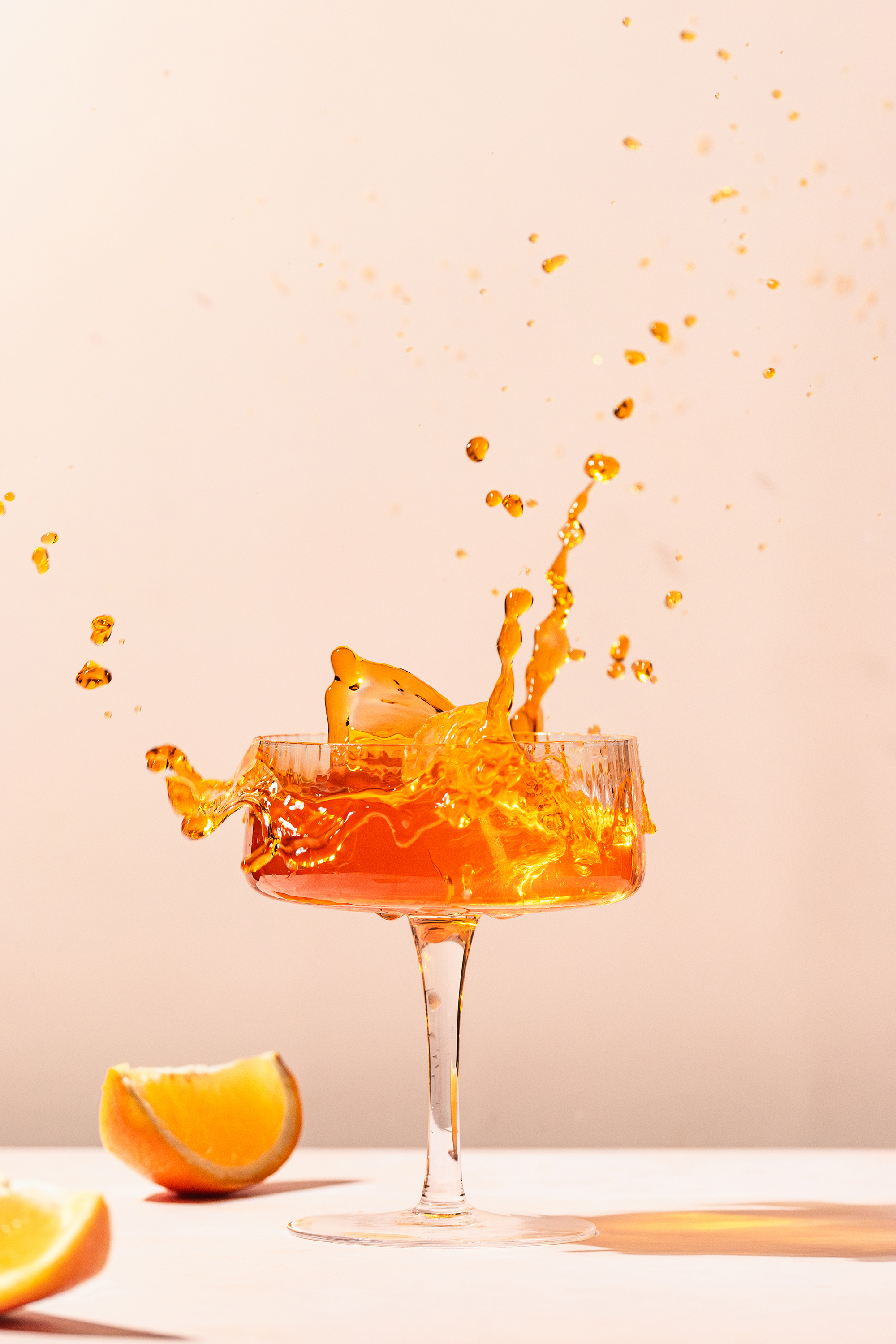 Kieliszek z pomarańczowym drinkiem i rozpryskującym się napojem na jasnym tle z kawałkami pomarańczy na stole.