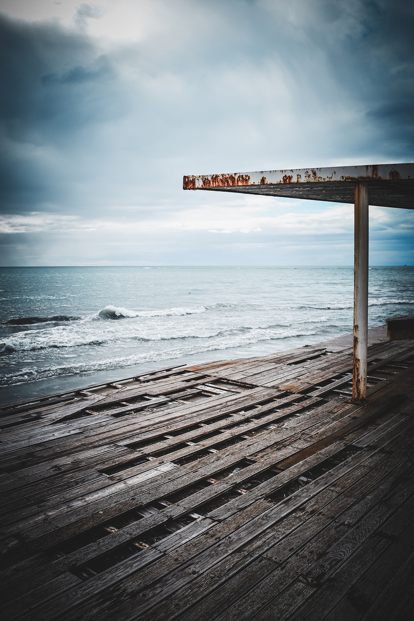 Zniszczony drewniany pomost nad morzem pod pochmurnym niebem.