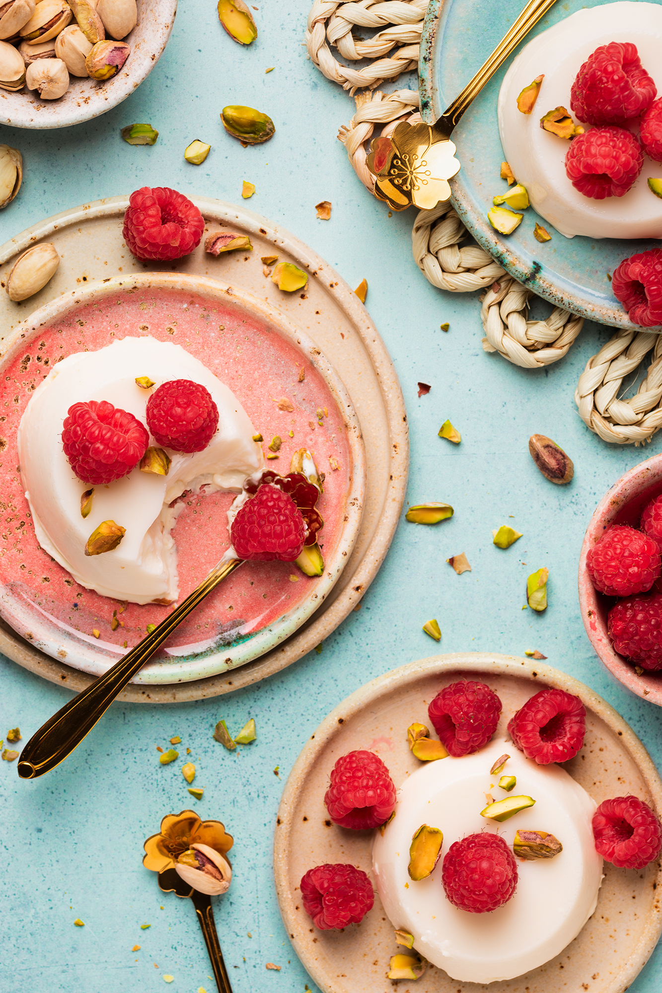 Deser panna cotta udekorowany świeżymi malinami i posiekanymi pistacjami na talerzach ceramicznych.